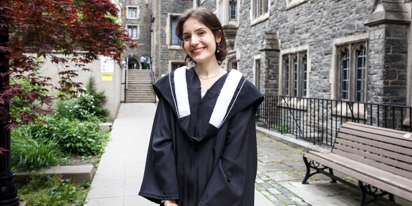 Faith Wershba standing near the gardens on Victoria College campus in her graduation gown.