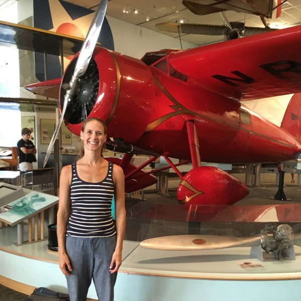 Author Lindsay Zier-Vogel standing in front of a red airplane at the Smithsonian. 