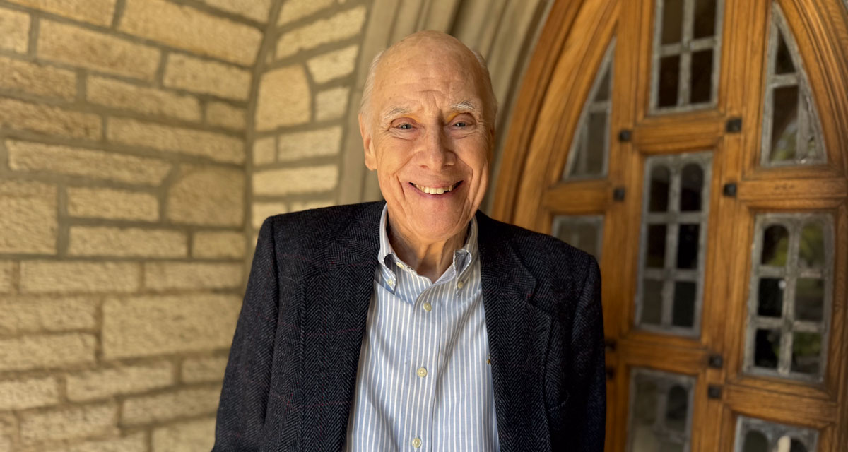 Richard Moffat smiles for the camera in front of a doorway outside the Emmanuel College building.