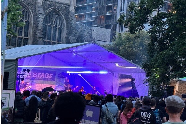 A live band delivers an electrifying performance on the main stage at The TD Toronto Jazz Festival, housed within a large tent in the scenic Burwash quad.