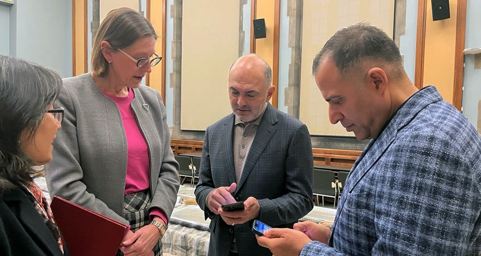 Emmanuel College Principal HyeRan Kim-Cragg and Louise Yearwood, executive director of Alumni Affairs & Advancement, watch as Rizwan Khalfan, president of the Board of Directors of the Islamic Shia Ithna-Asheri Jamaat of Toronto, and treasurer Amin Kermali, check an app developed by the ISIJ to advise Muslims when the sun has set and they can break the Ramadan fast.