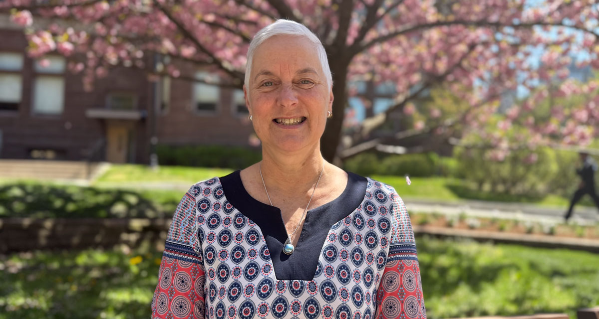 Deb Walker smiles for the camera in front of a cherry blossom tree on Victoria University campus.