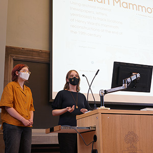 Two masked students standing at a podium doing a presentaiton.  